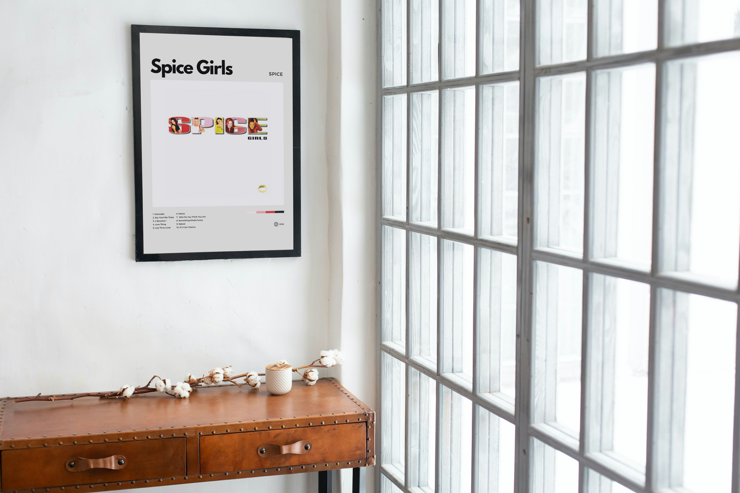 Framed Spice Girls poster on a wall next to a wooden desk with decor items.