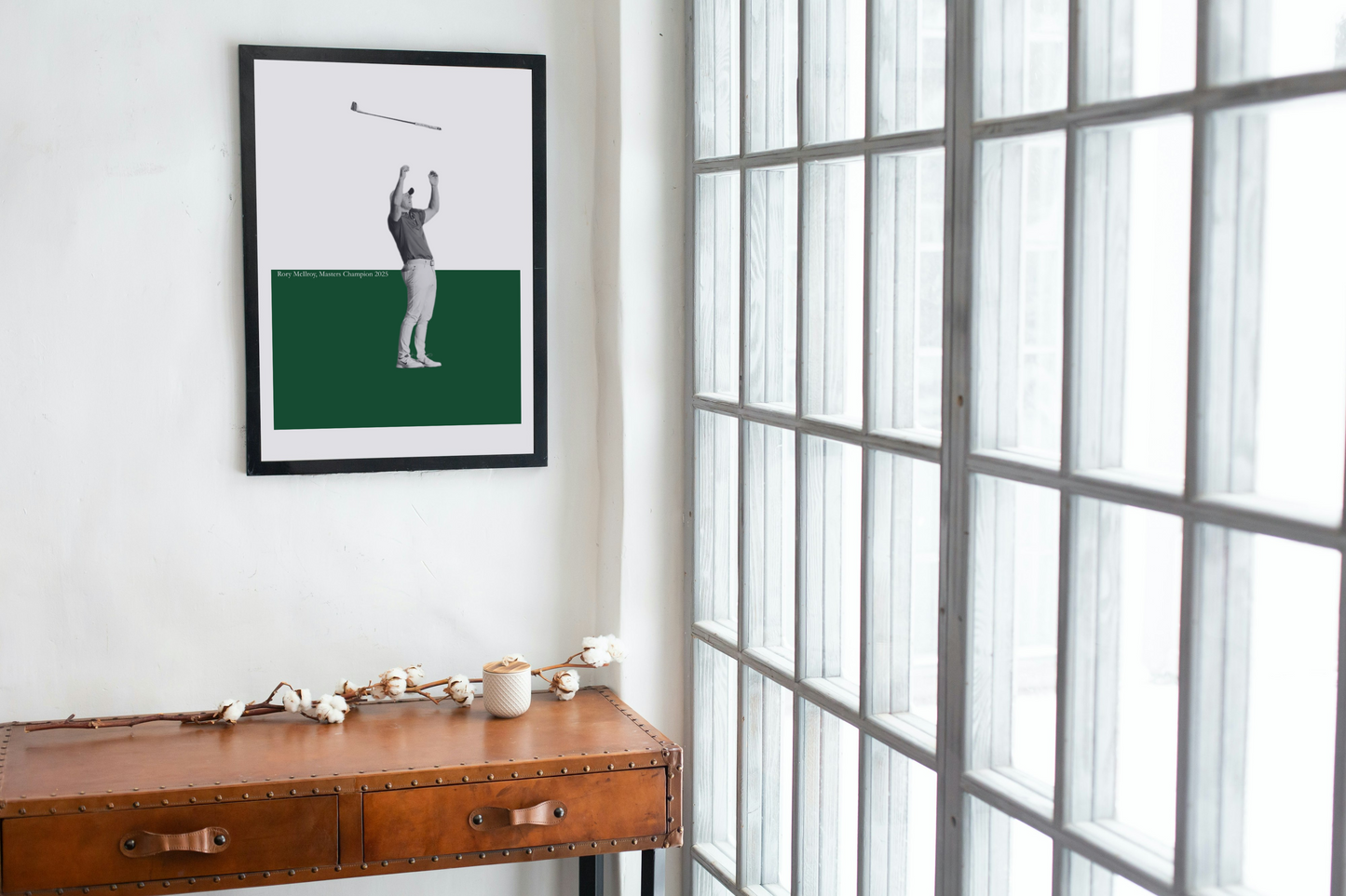 Framed picture of Rory McIlroy on a green background above a wooden desk with a window in the background.