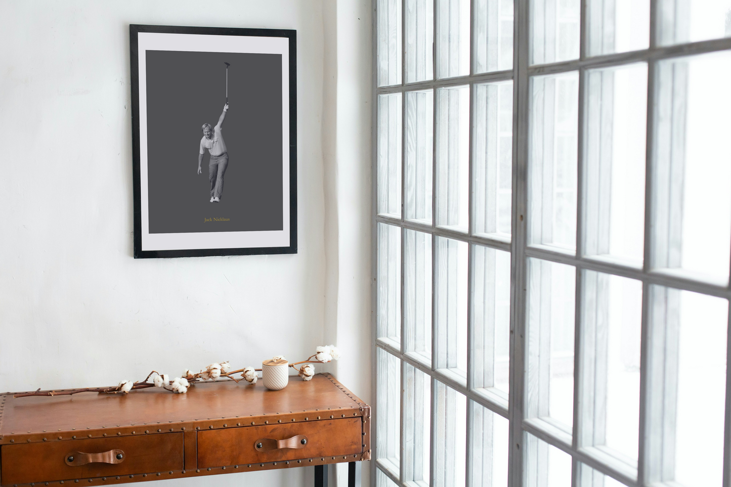 Framed artwork on a wall above a wooden desk with a large window in the background.