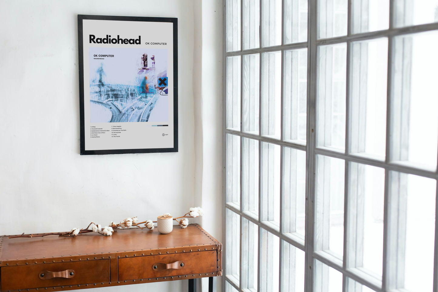 Framed Radiohead album cover on a wall next to a wooden desk with decor items.