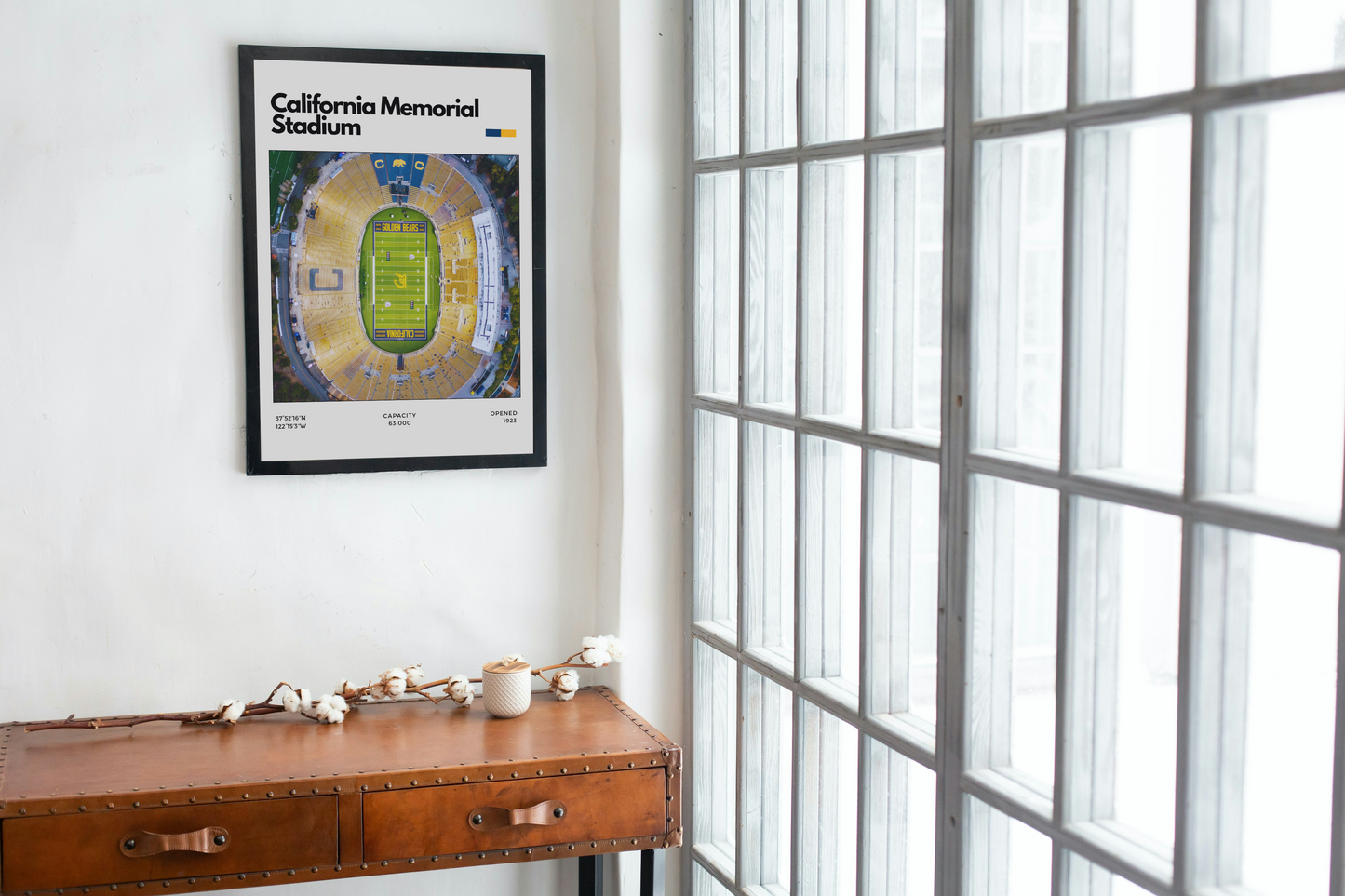Framed poster of California Memorial Stadium on a wall next to a wooden desk with decor items.