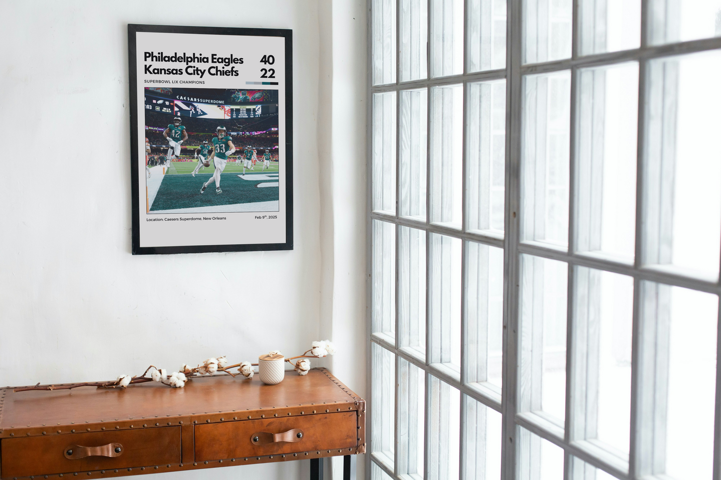 Framed sports poster of Philadelphia Eagles vs Kansas City Chiefs on a wall above a wooden desk.