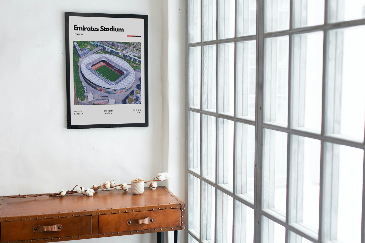 Framed poster of Emirates Stadium on a wall next to a window.