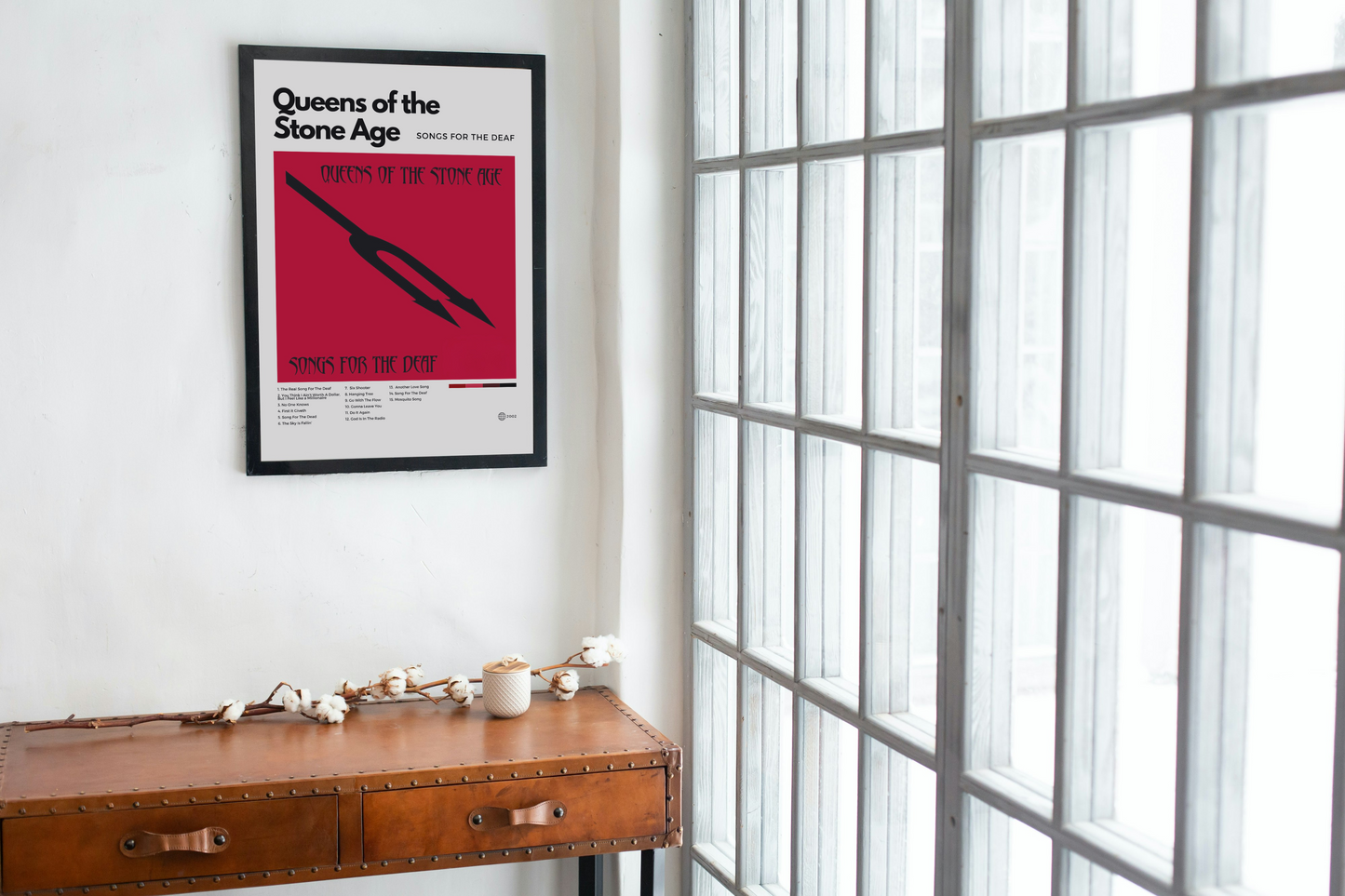 Framed Queens of the Stone Age poster on a wall above a wooden desk.