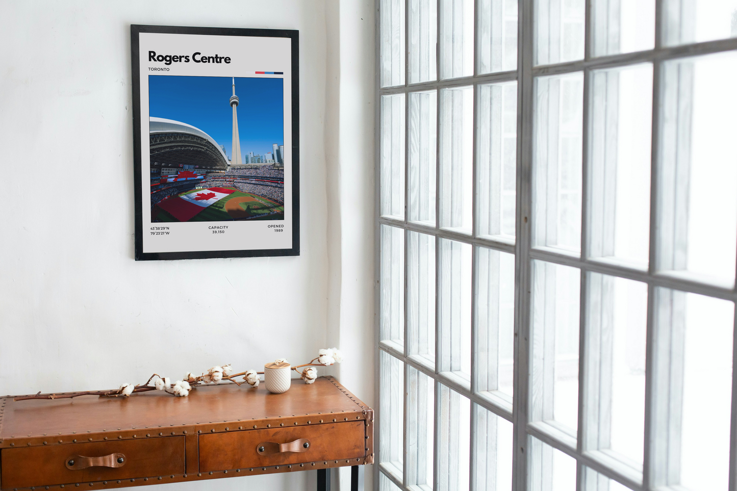 Framed poster of the Rogers Centre on a wall next to a window.
