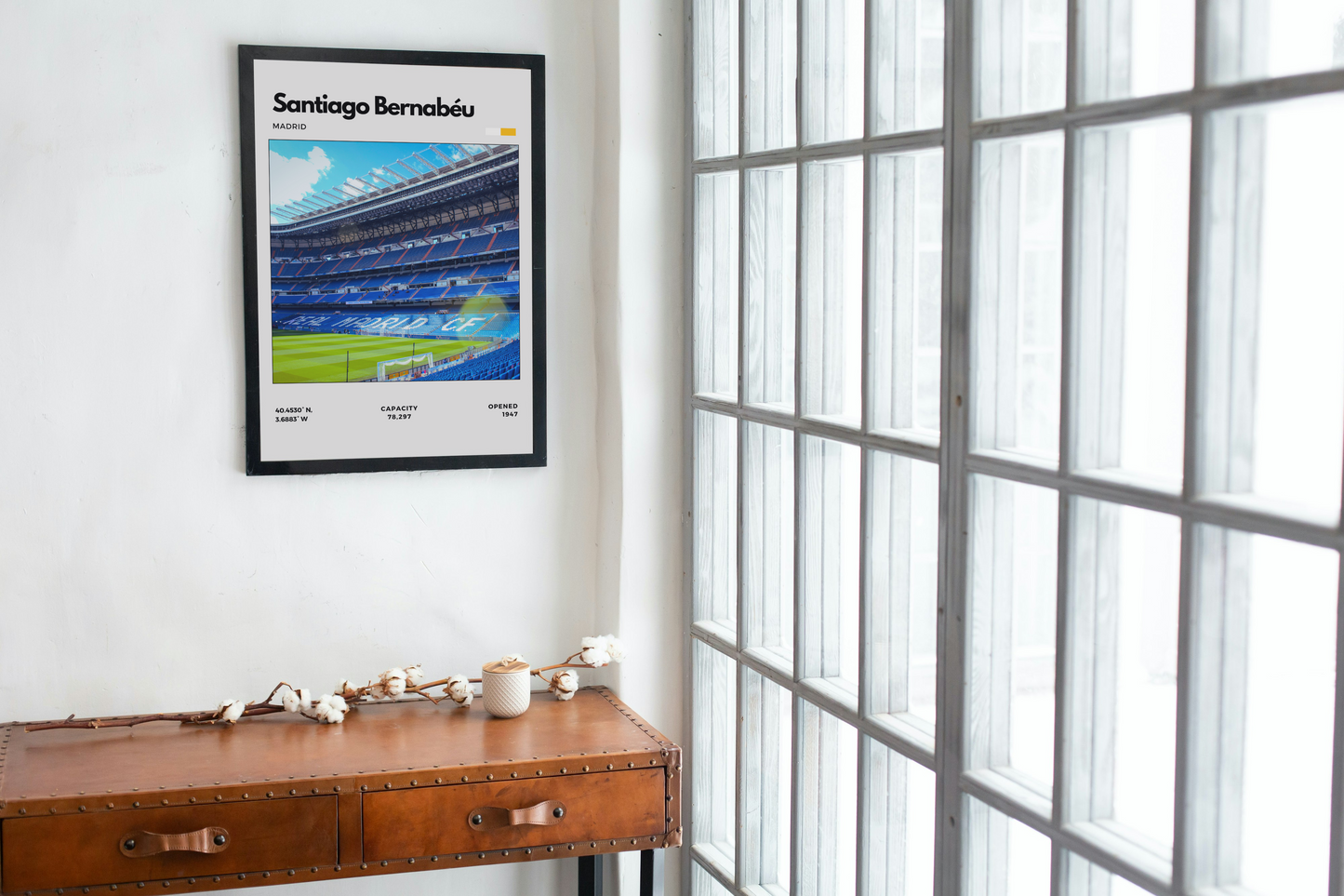 Framed poster of Santiago Bernabéu stadium on a wall next to a wooden desk.