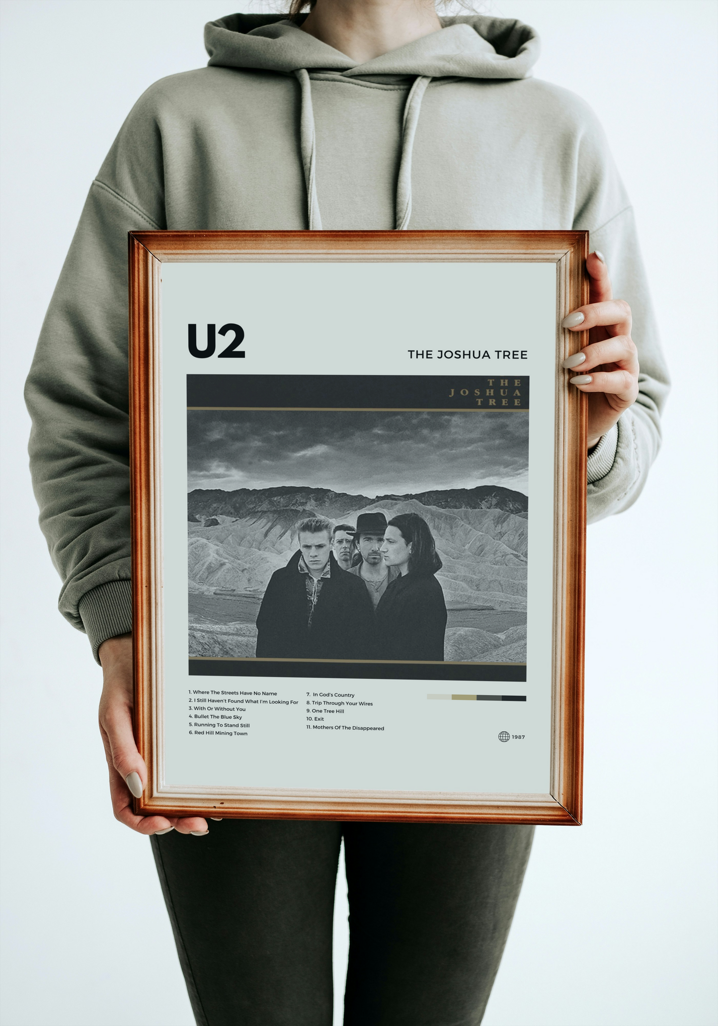 Person holding a framed U2 'The Joshua Tree' album cover against a white background
