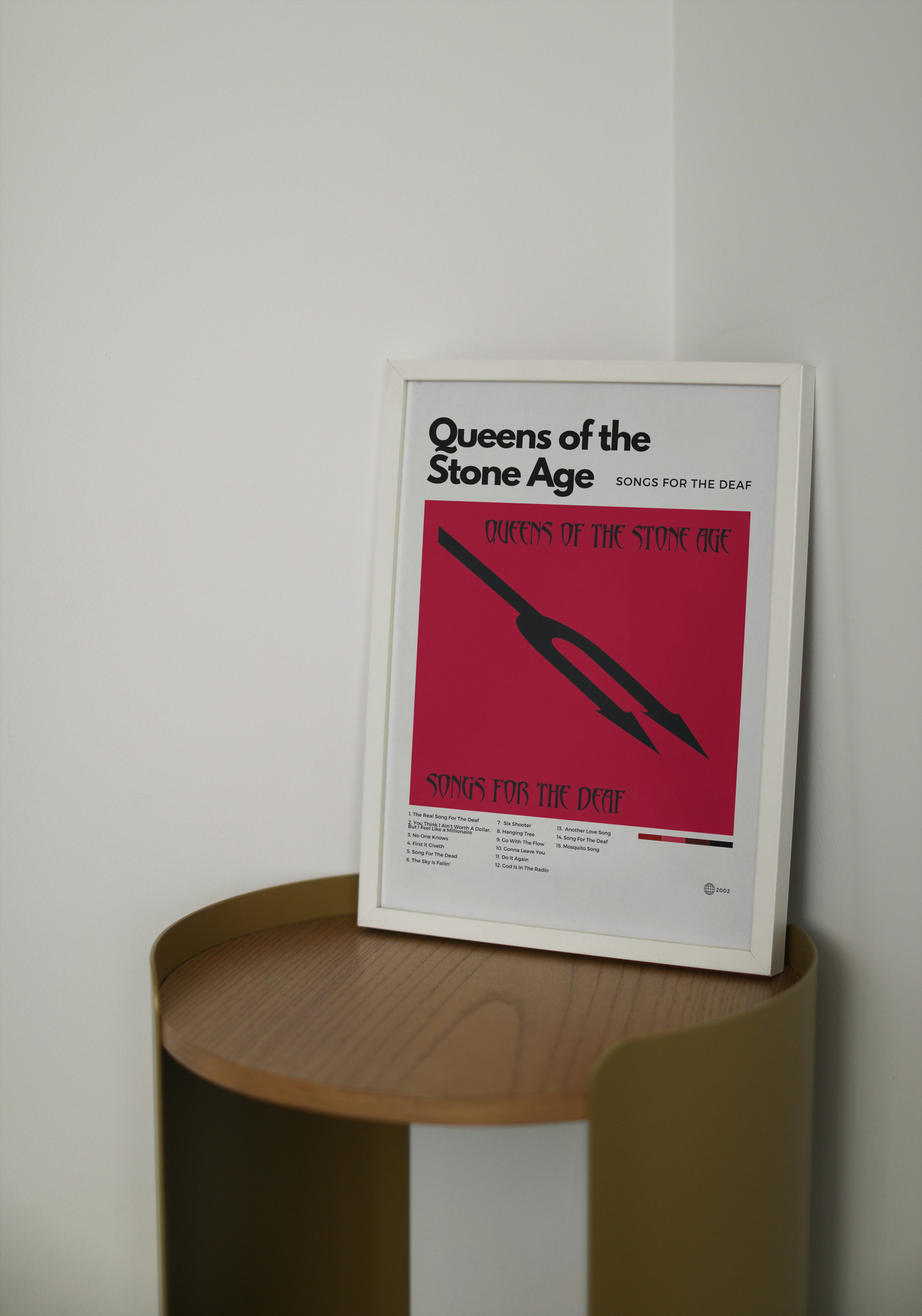 Framed Queens of the Stone Age poster on a wooden shelf against a white wall