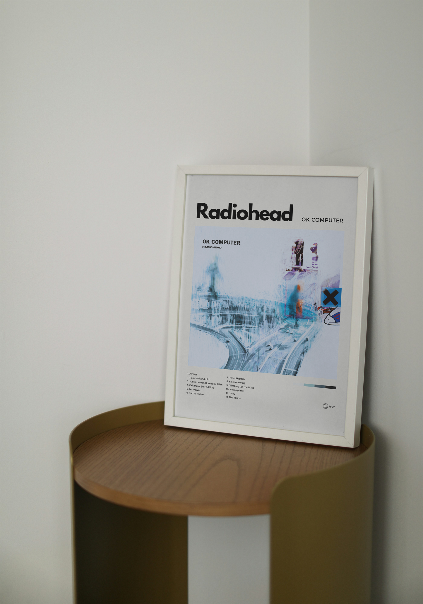 Framed Radiohead album cover on a wooden side table against a white wall