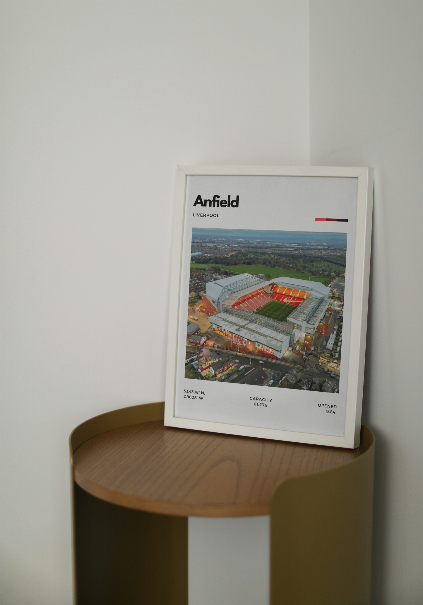Framed poster of Anfield stadium on a wooden shelf against a white wall