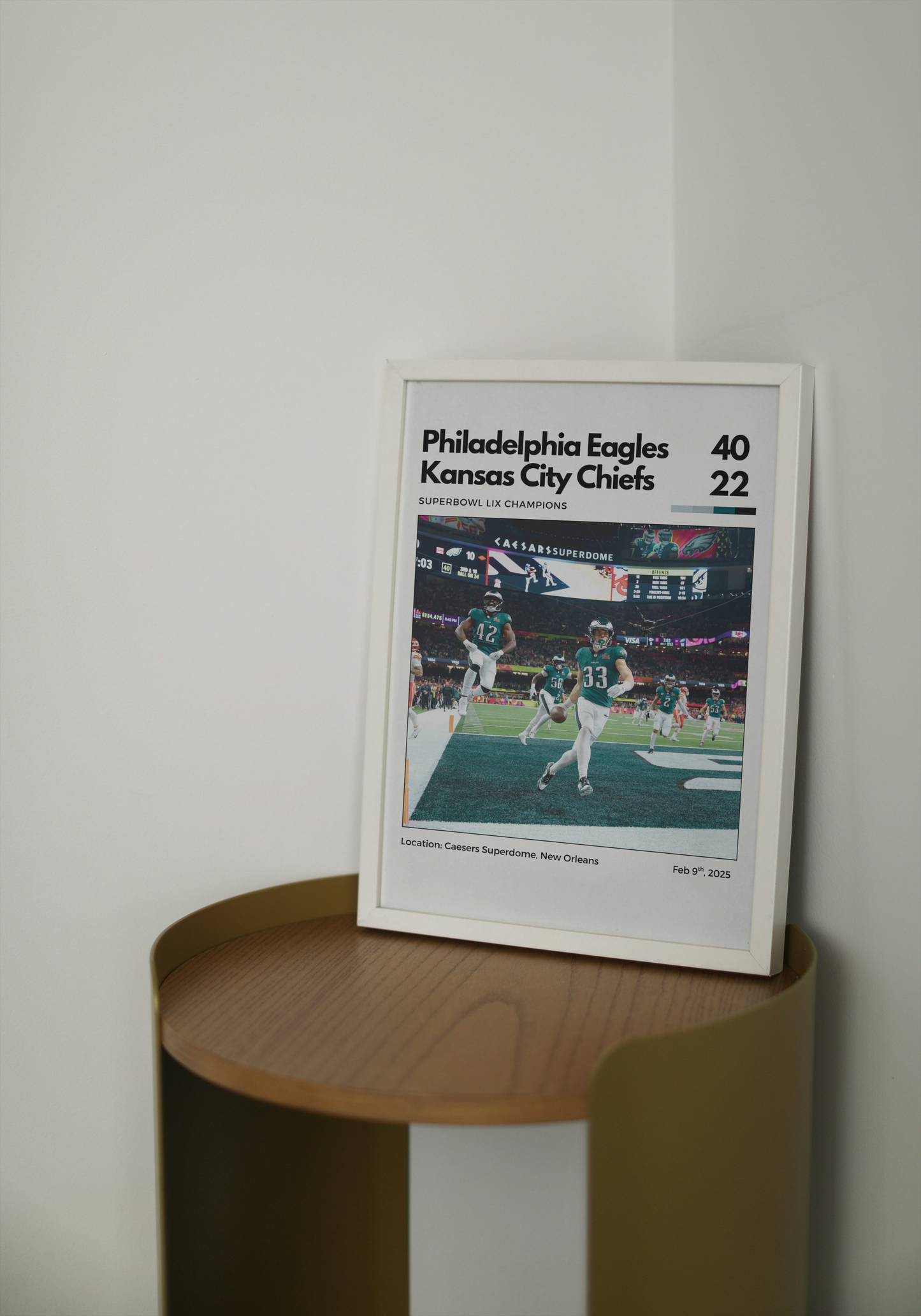 Framed sports poster of Philadelphia Eagles vs Kansas City Chiefs game on a wooden shelf.
