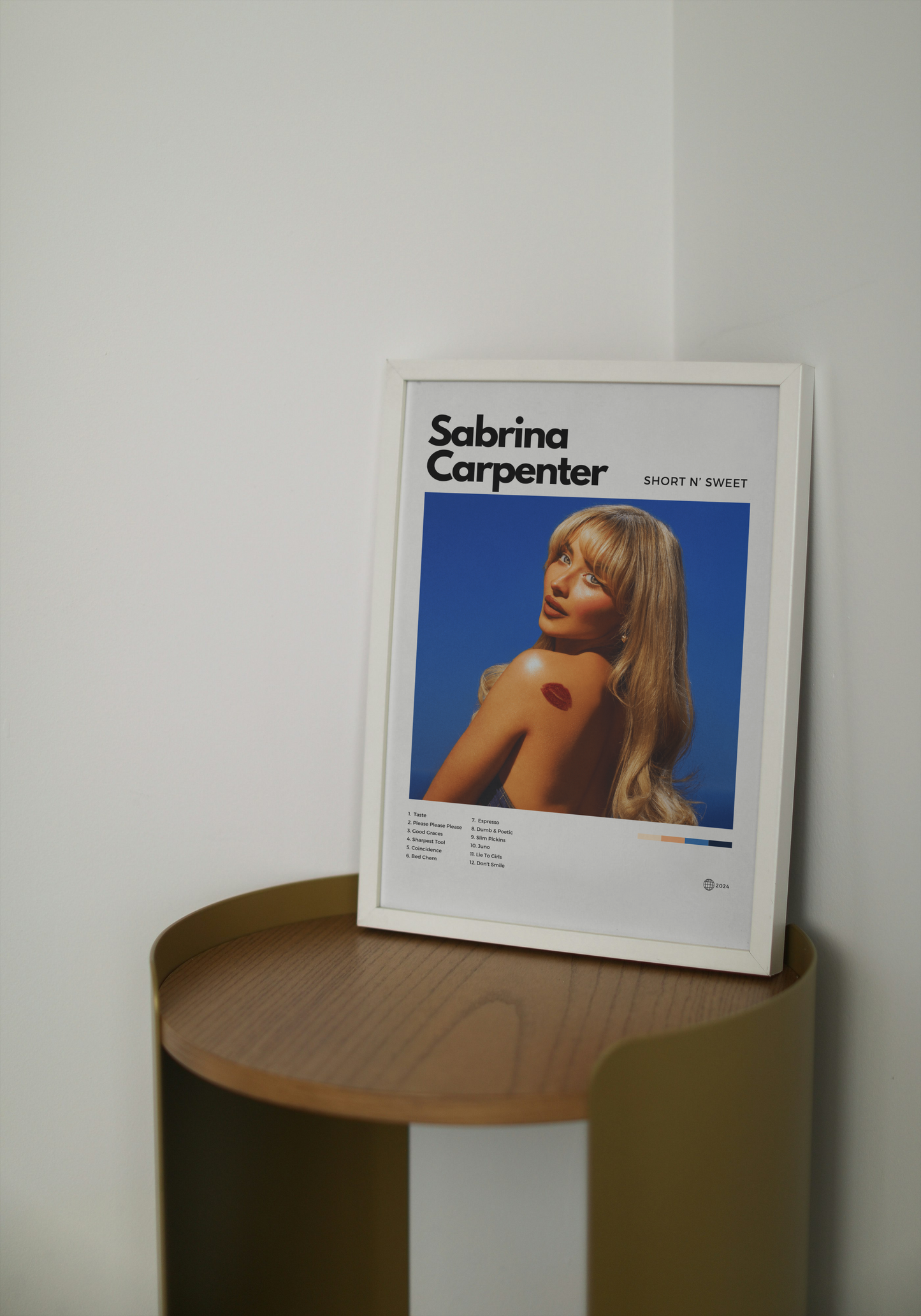 Framed poster of Sabrina Carpenter on a wooden side table against a white wall.