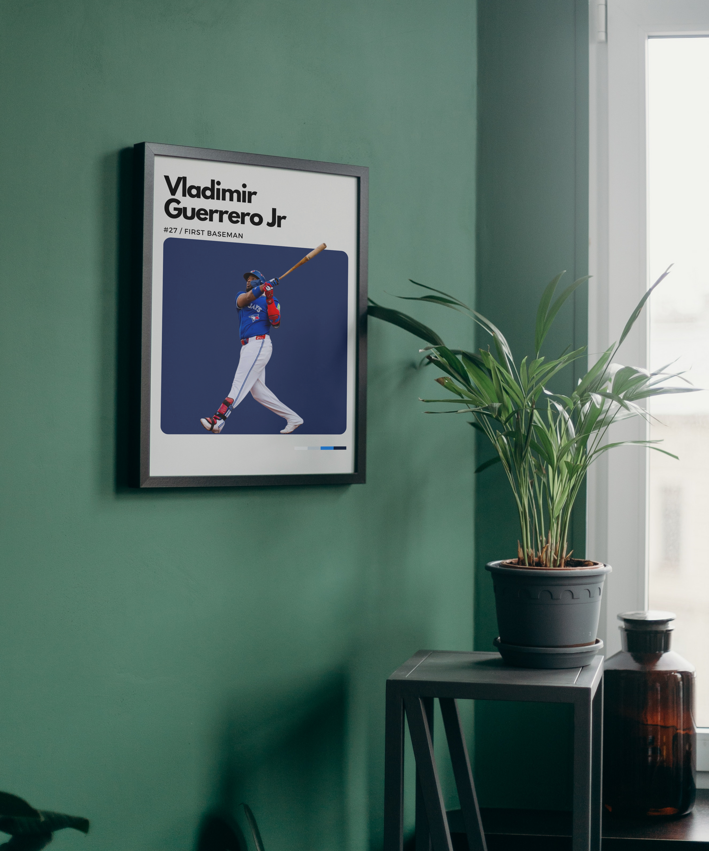 Framed poster of Vladimir Guerrero Jr. on a green wall with a plant and bottle in the background.