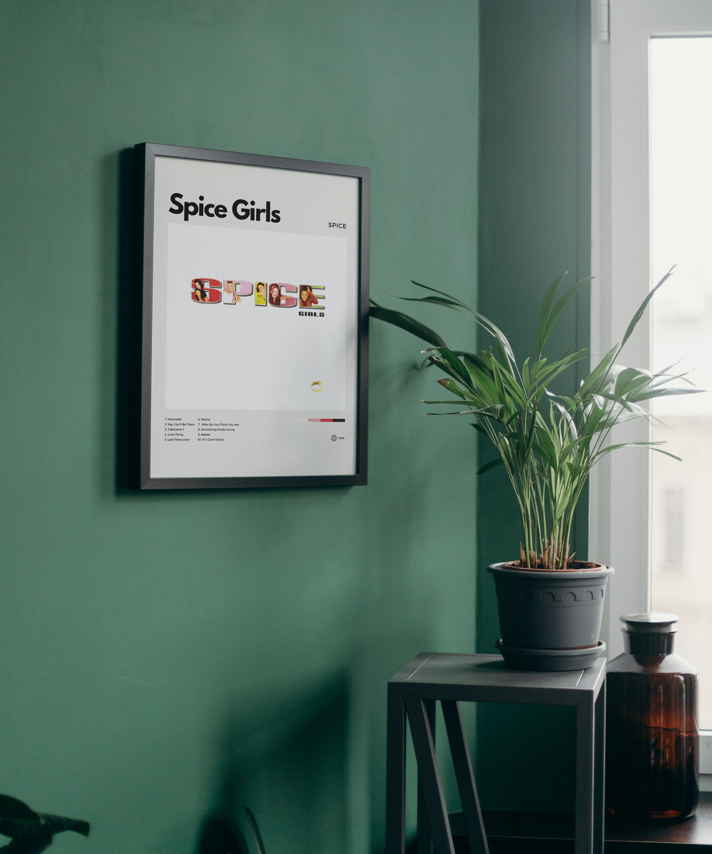Framed Spice Girls poster on a green wall with a plant and bottle in the foreground.