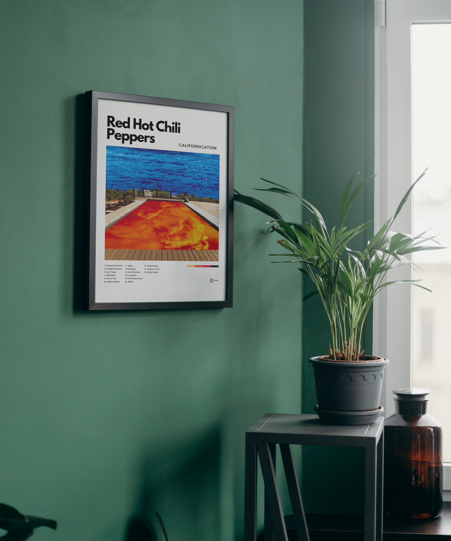 Framed poster of Red Hot Chili Peppers album on a green wall with a plant and bottle in the foreground.