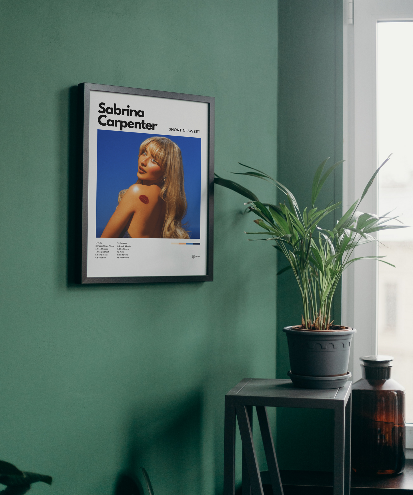 Framed poster of Sabrina Carpenter on a green wall with a plant and bottle in the background.