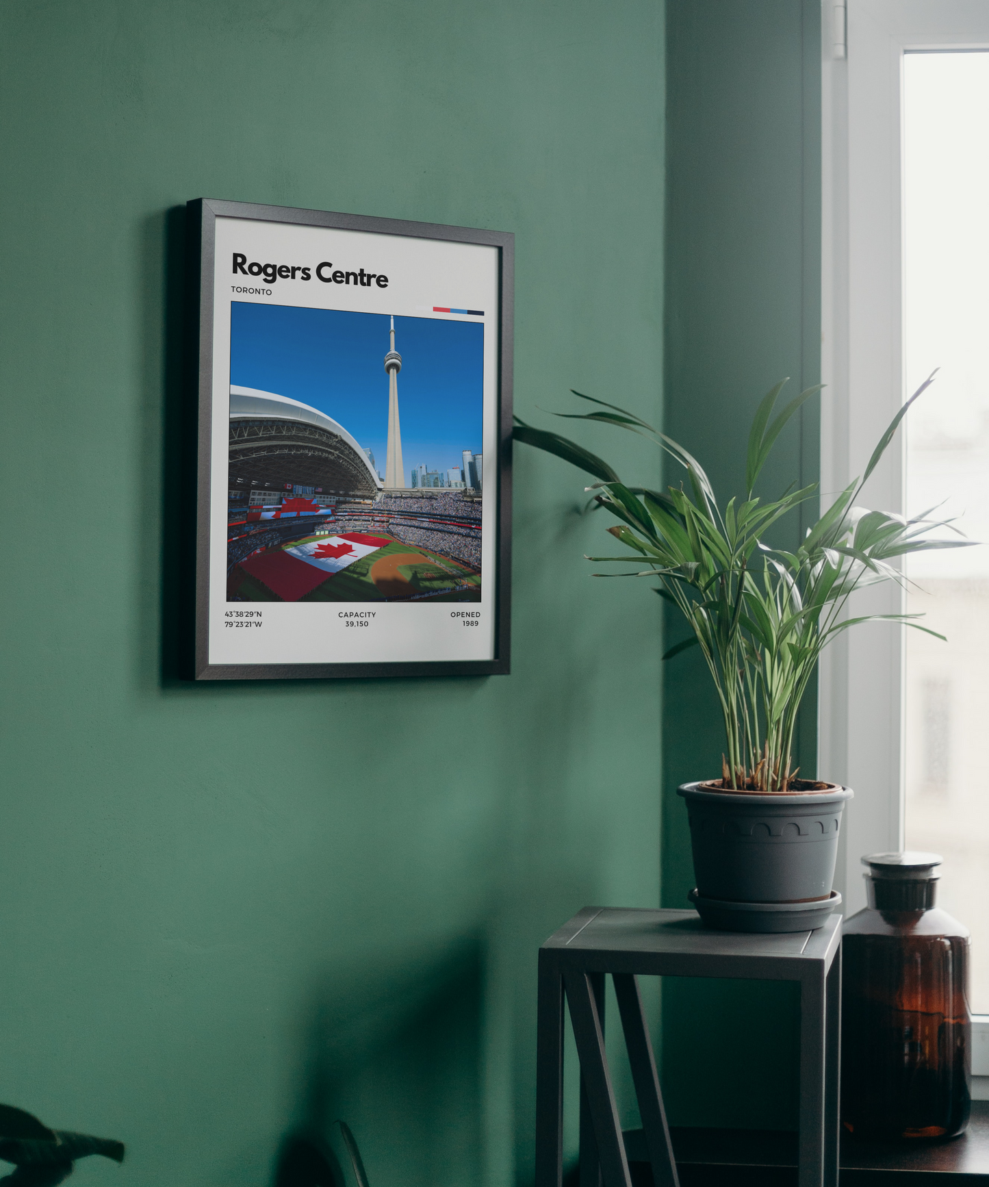 Framed poster of Rogers Centre on a green wall with a plant and bottle in the foreground.