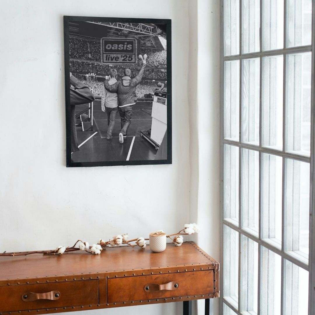 Framed concert poster of Oasis on a wall above a wooden console table.