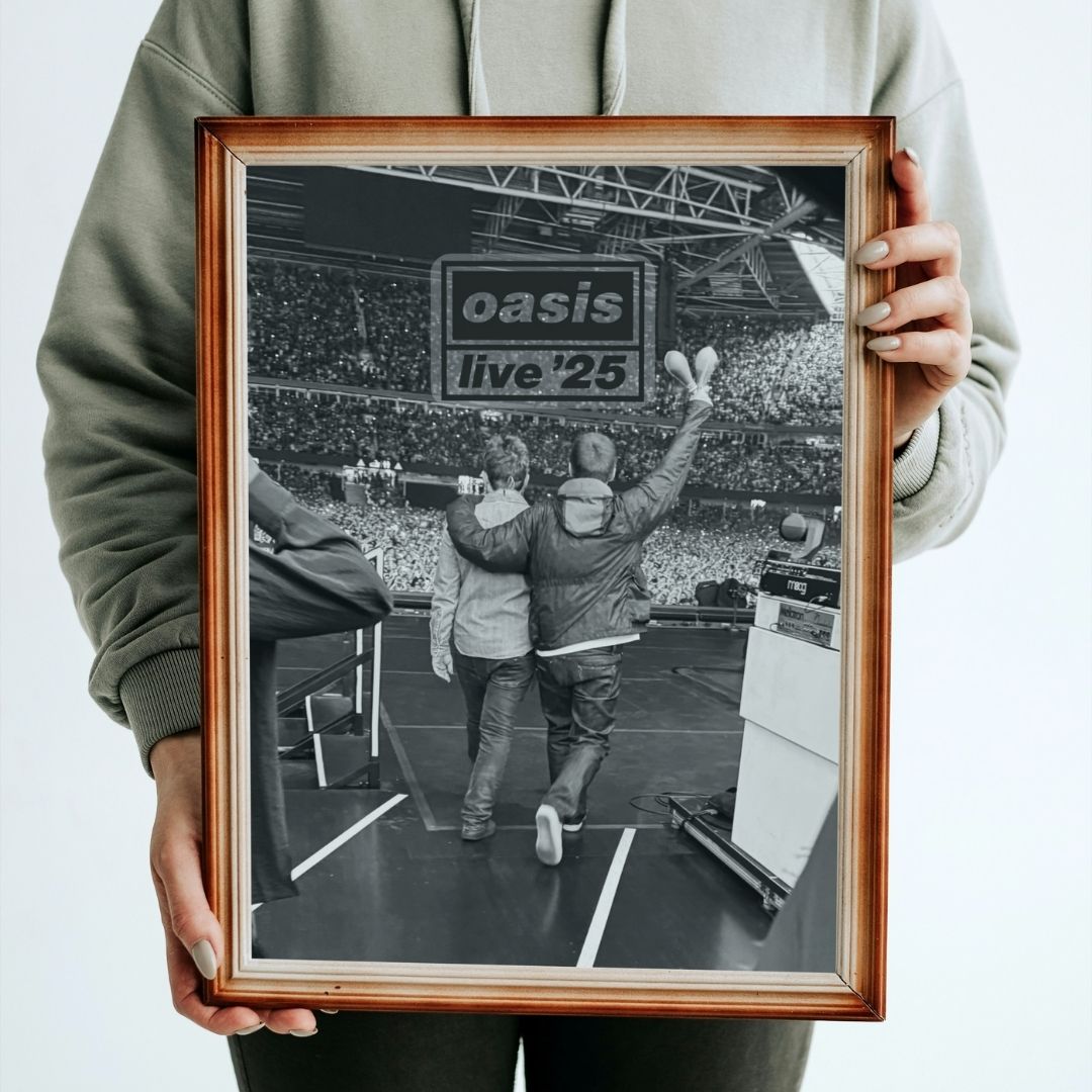 Person holding a framed photograph of two people on stage with 'oasis live '25' text.