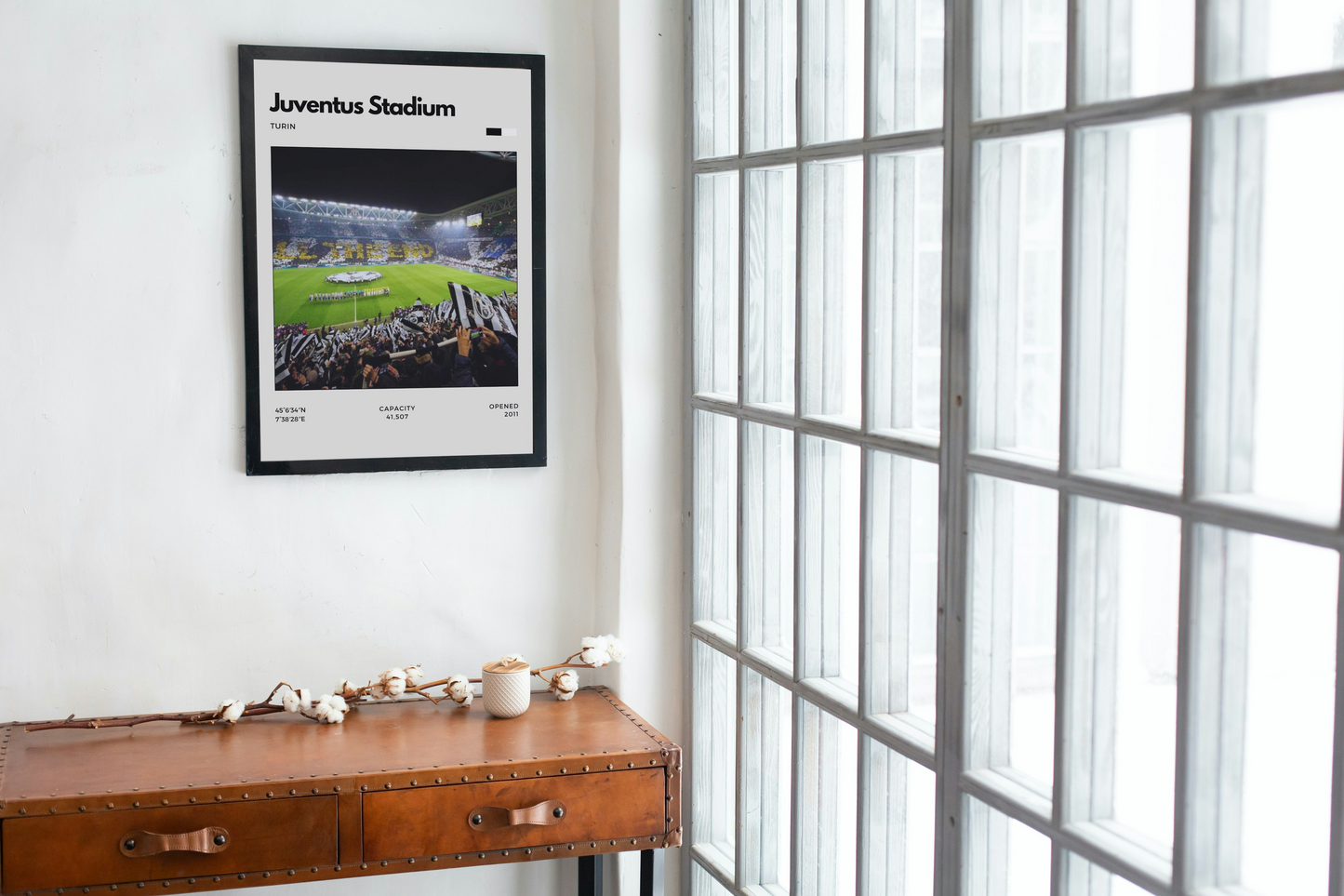 Framed poster of Juventus Stadium on a wall above a wooden desk.