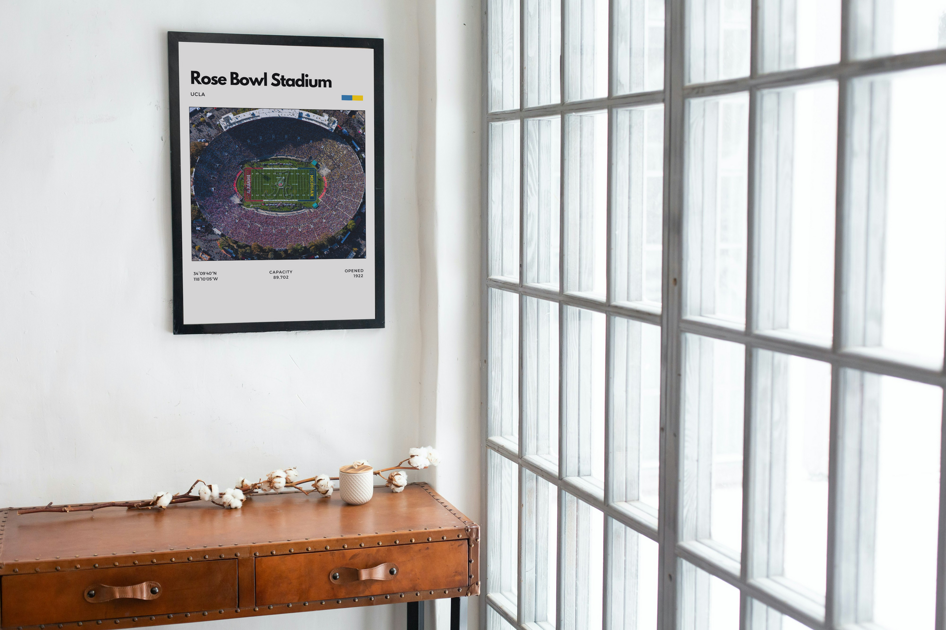 Framed poster of Rose Bowl Stadium on a wall next to a wooden desk with decor items.