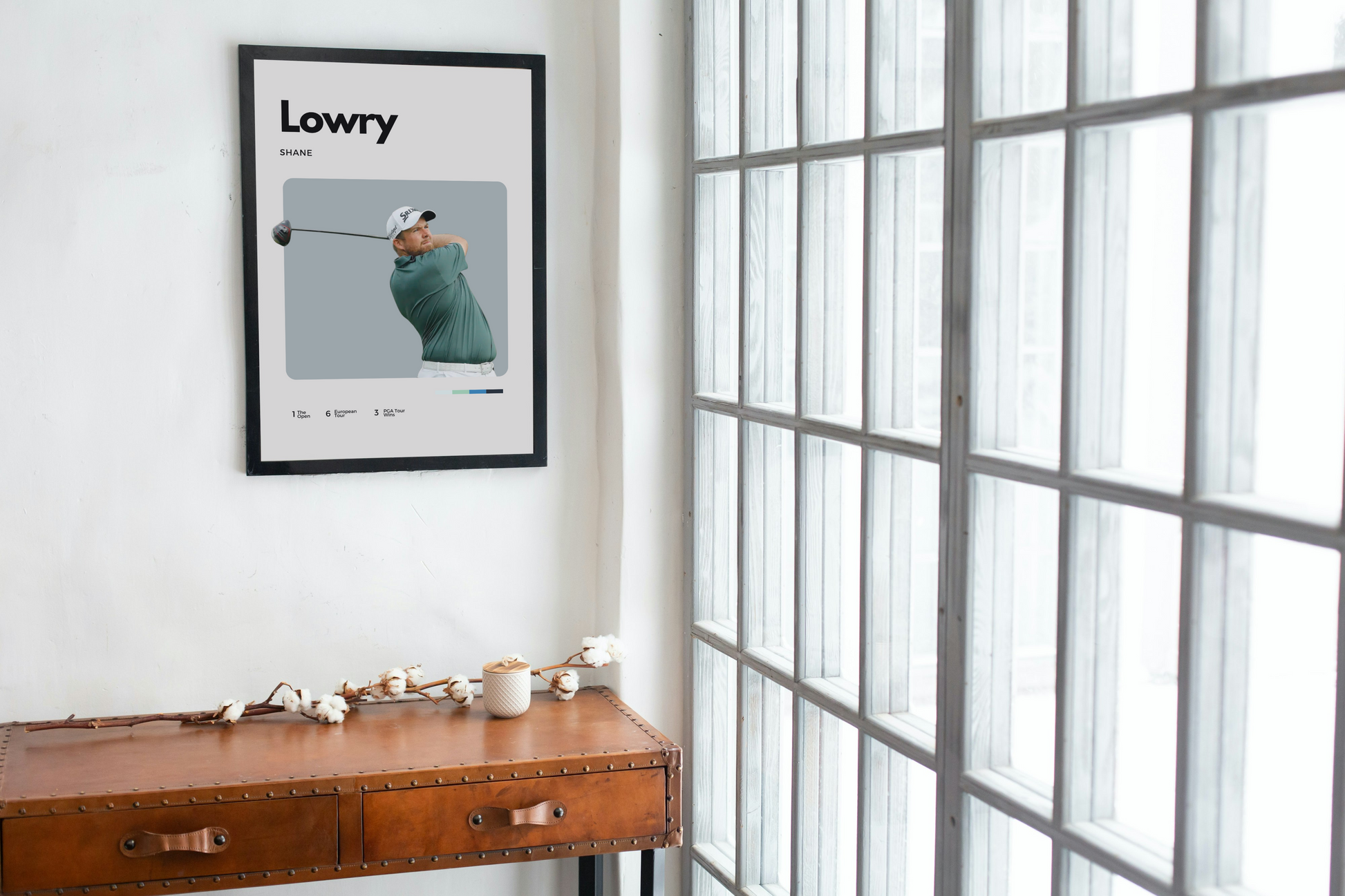 Framed poster of a golfer on a wall above a wooden desk with a window in the background.