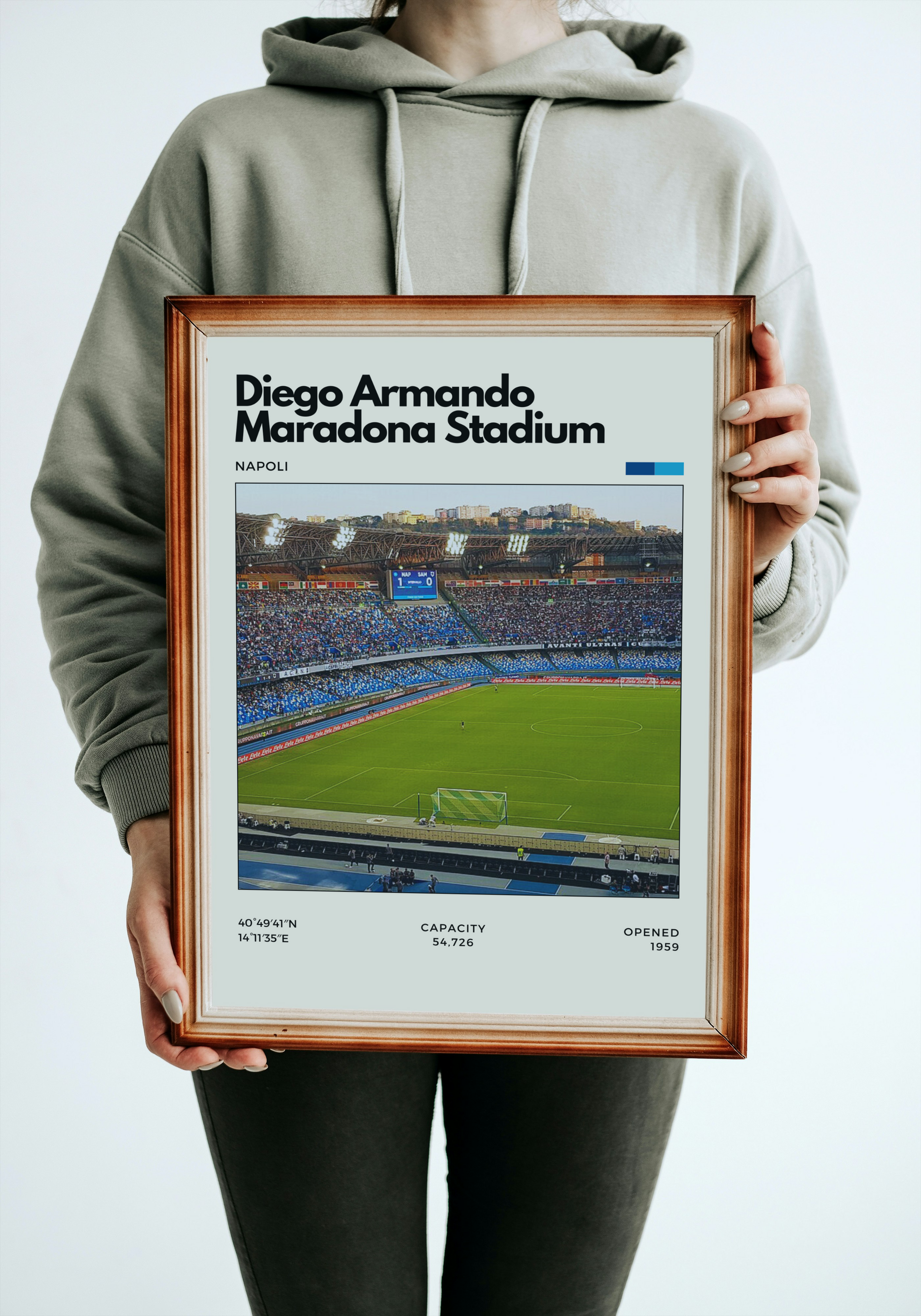 Person holding Poster of Diego Armando Maradona Stadium in Naples, Italy, showing a full crowd with blue seating and green pitch under bright stadium lights.