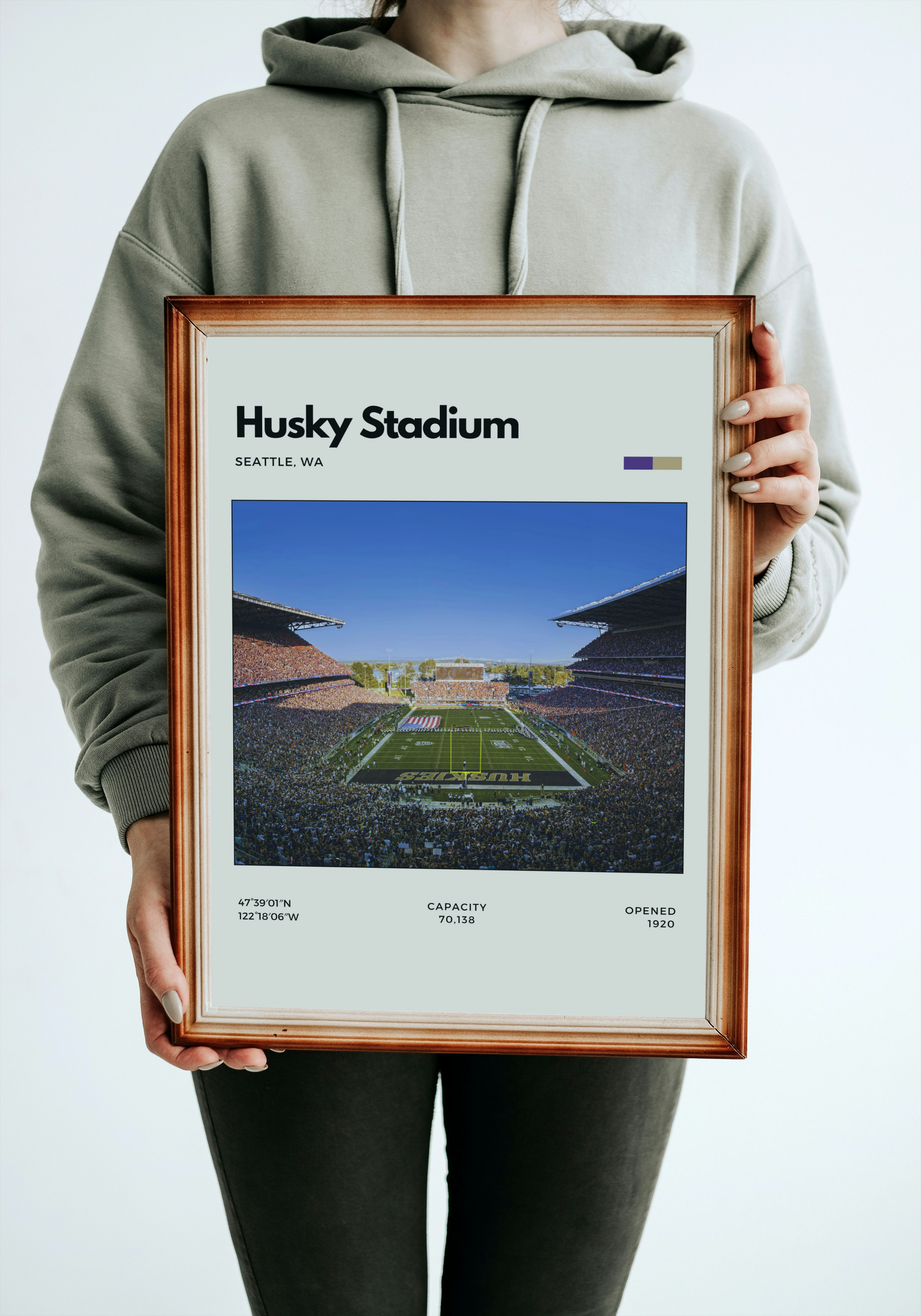 Person holding a framed print of Husky Stadium with a gray hoodie.