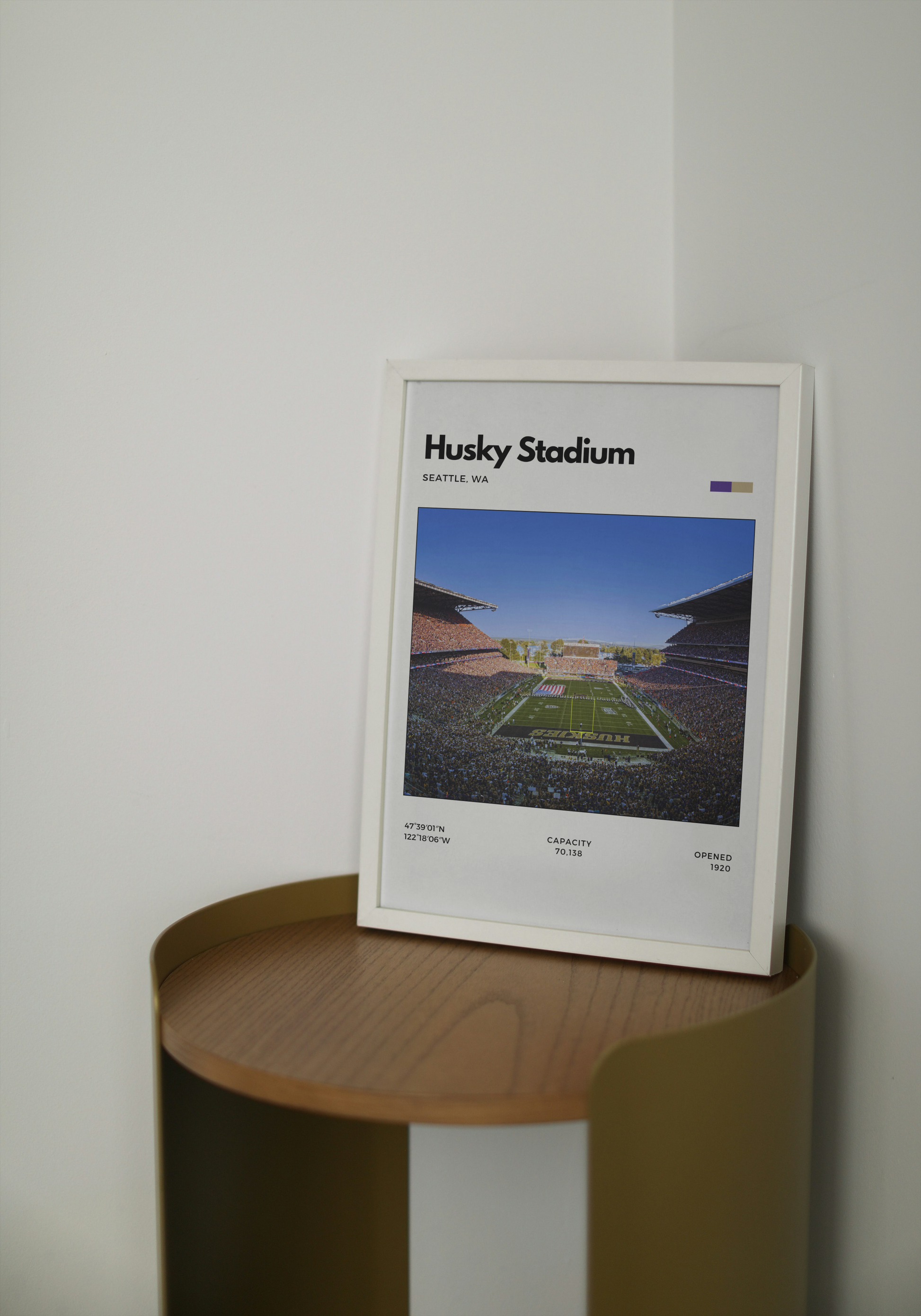 Framed poster of Husky Stadium on a wooden shelf against a white wall