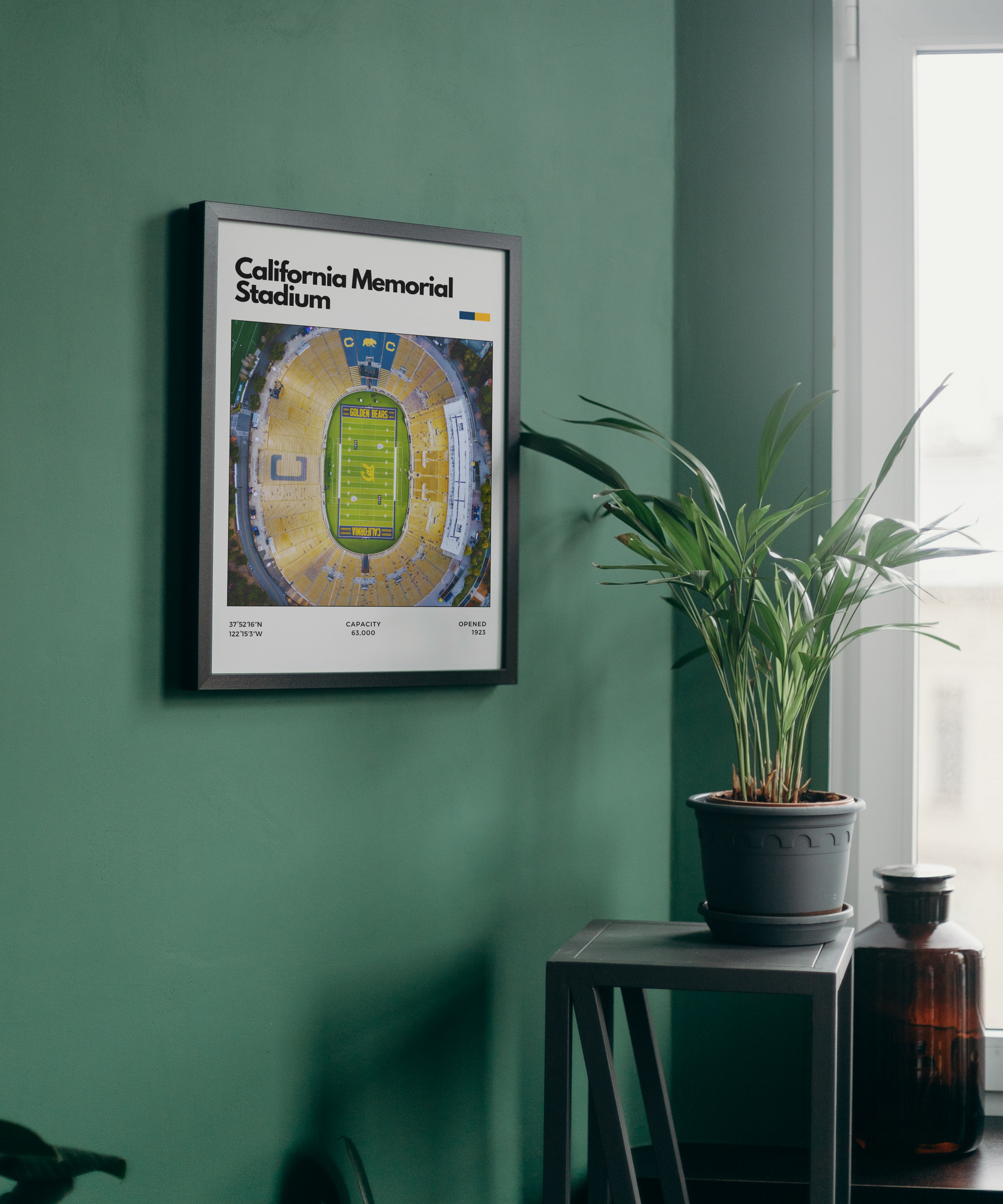 Framed poster of California Memorial Stadium on a green wall with a plant and bottle in the foreground.