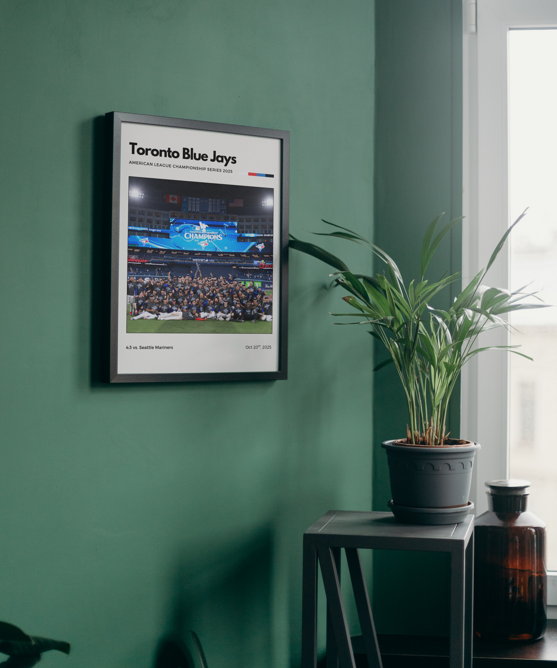 Framed Toronto Blue Jays poster on a green wall with a plant and bottle in the foreground.
